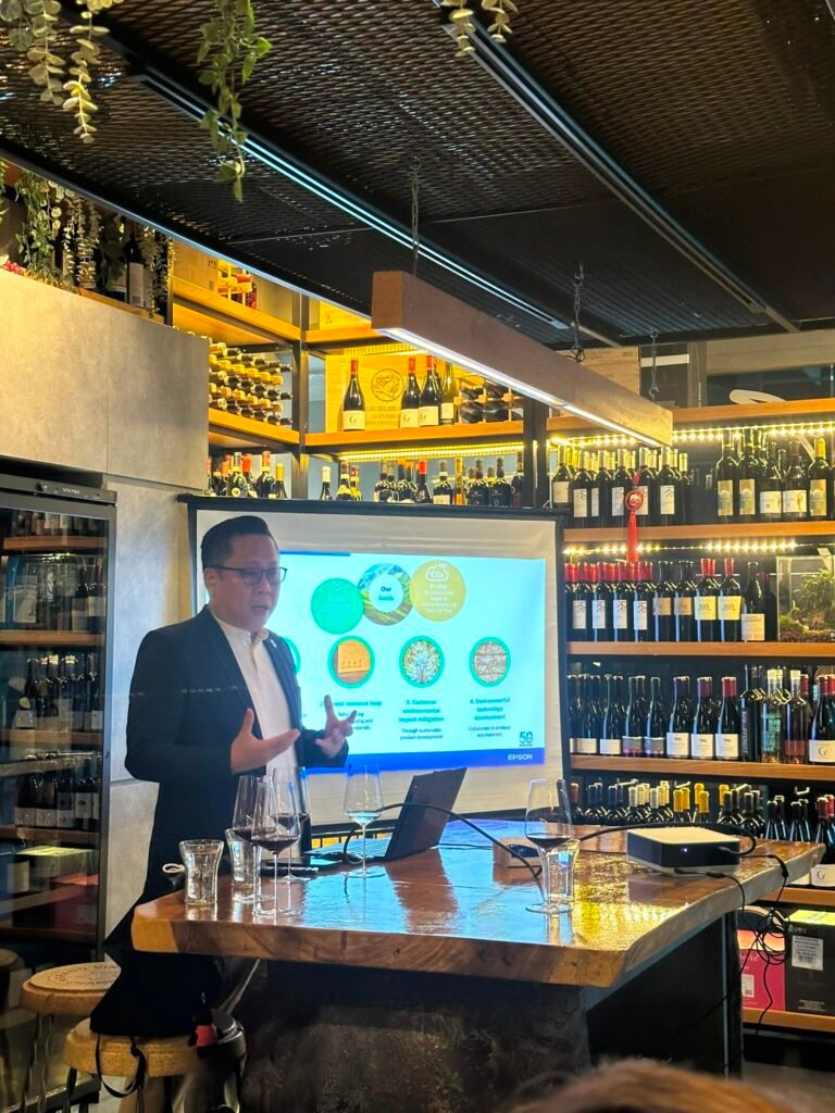 A man presents in a wine cellar, using a projector screen displaying his goals